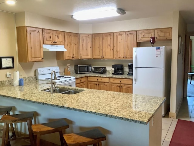 kitchen with white appliances, a breakfast bar area, light tile patterned floors, a peninsula, and under cabinet range hood