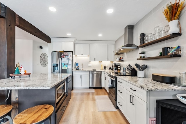 kitchen featuring light wood finished floors, light stone counters, wall chimney range hood, a sink, and appliances with stainless steel finishes