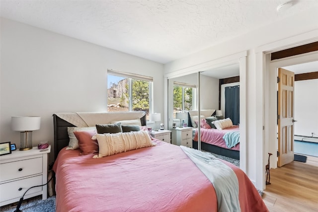 bedroom featuring a baseboard radiator, a closet, a textured ceiling, and light wood-type flooring