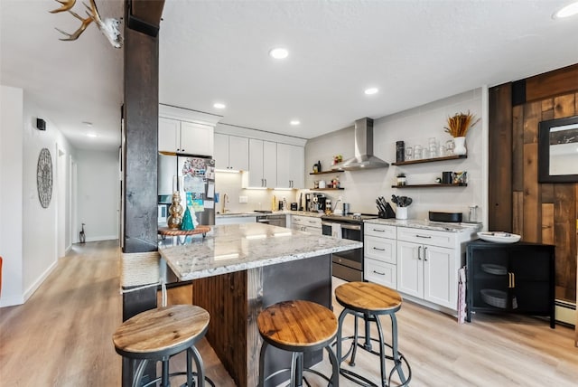 kitchen with open shelves, light wood-style floors, wall chimney range hood, and stainless steel appliances