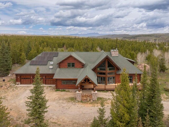 12000 Ute Pass Rd, Parshall, CO 80468 - view of front facade featuring a wooded view, driveway, log exterior, solar panels, and a chimney