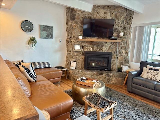 living area featuring beam ceiling, a stone fireplace, and wood finished floors