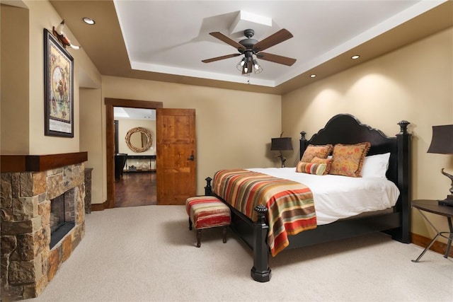 bedroom featuring carpet flooring, baseboards, a stone fireplace, and a raised ceiling