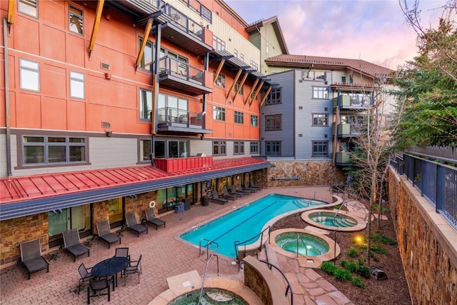 pool at dusk featuring a community pool, a fenced backyard, a community hot tub, and a patio area