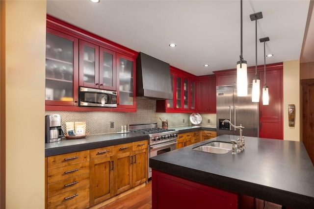 kitchen featuring high end appliances, dark countertops, wall chimney exhaust hood, a sink, and decorative light fixtures