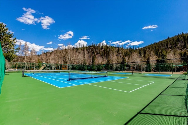 view of tennis court featuring fence and a view of trees