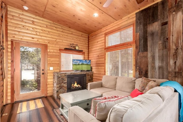 living room with log walls, wooden ceiling, wood finished floors, and a lit fireplace