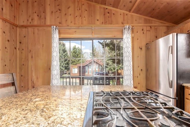 kitchen with freestanding refrigerator, wooden walls, lofted ceiling, wood ceiling, and light stone countertops