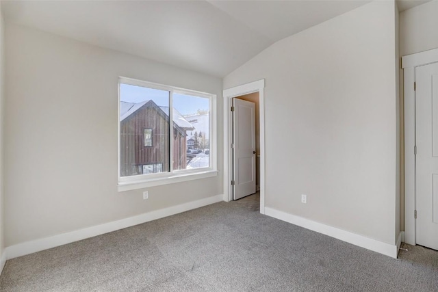 carpeted spare room featuring vaulted ceiling and baseboards