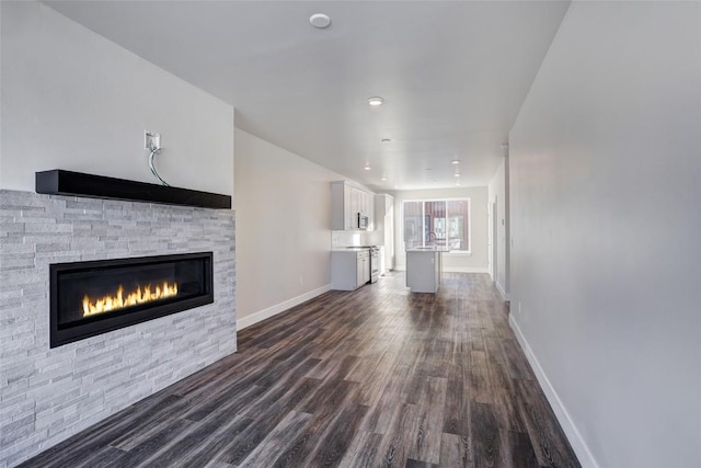 unfurnished living room with a sink, dark wood-style flooring, baseboards, recessed lighting, and a stone fireplace