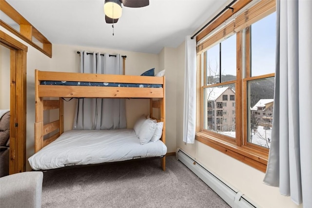 carpeted bedroom with a baseboard heating unit, ceiling fan, and multiple windows