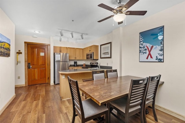 dining area with light wood-type flooring, rail lighting, a ceiling fan, and baseboards