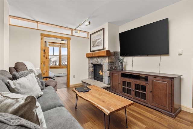 living room featuring track lighting, a baseboard heating unit, baseboards, a fireplace, and light wood-style flooring