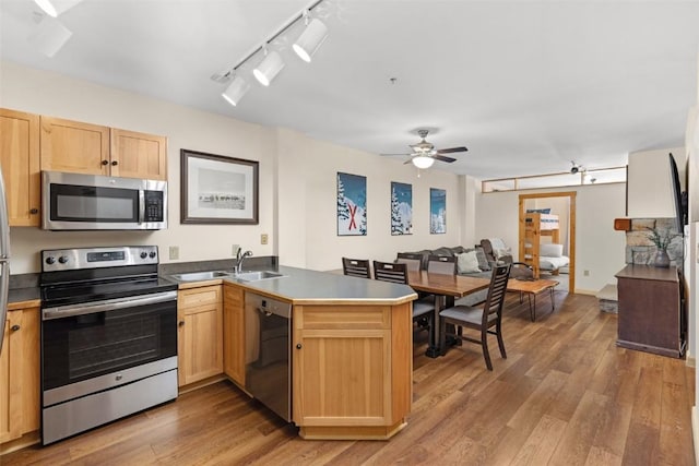 kitchen with light brown cabinets, a sink, light wood-style flooring, a peninsula, and appliances with stainless steel finishes