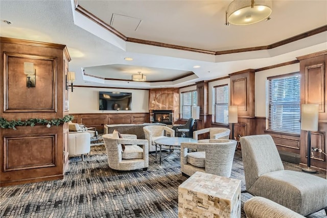 carpeted living room with a tray ceiling, wooden walls, a large fireplace, and ornamental molding