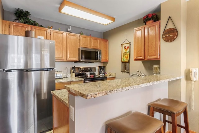 kitchen featuring kitchen peninsula, appliances with stainless steel finishes, light stone countertops, and a breakfast bar area