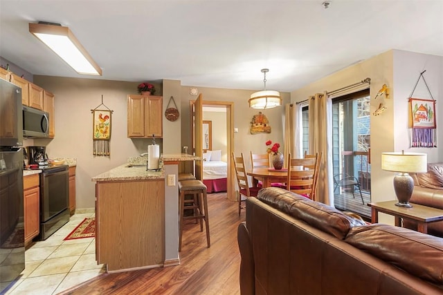 kitchen featuring light stone countertops, appliances with stainless steel finishes, decorative light fixtures, kitchen peninsula, and a breakfast bar area