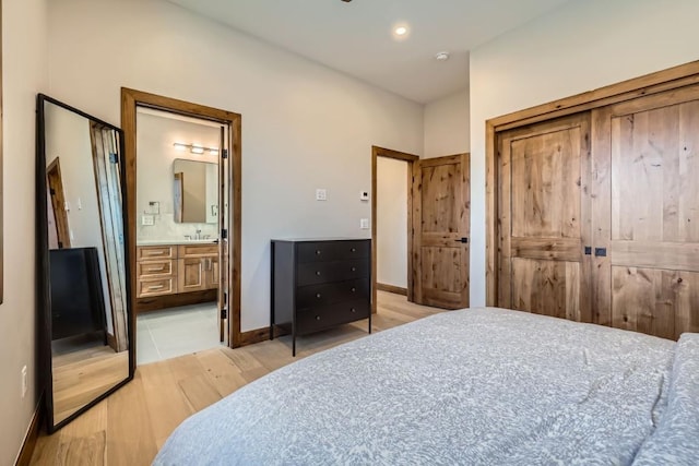 bedroom with light wood-type flooring, sink, and ensuite bath