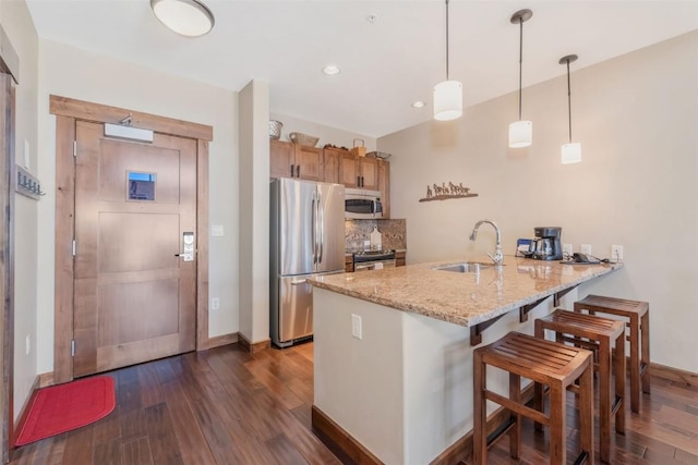 kitchen featuring stainless steel appliances, a peninsula, a sink, dark wood finished floors, and baseboards
