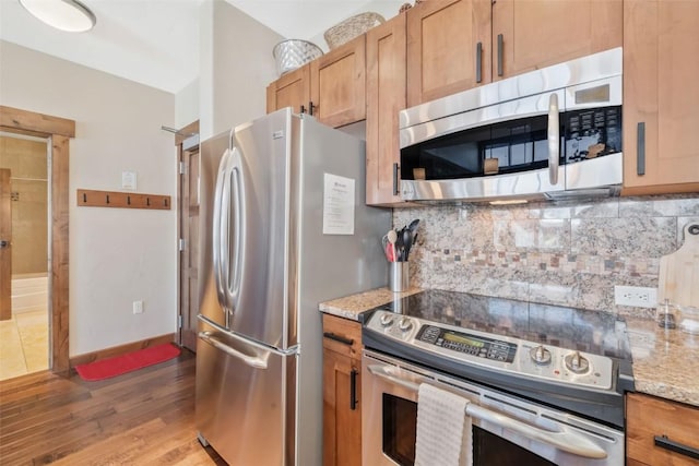 kitchen with tasteful backsplash, wood finished floors, stainless steel appliances, baseboards, and light stone countertops