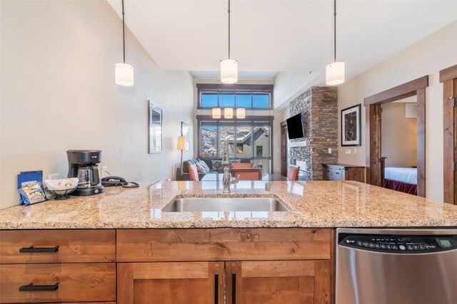 kitchen featuring stainless steel dishwasher, pendant lighting, a sink, and light stone counters