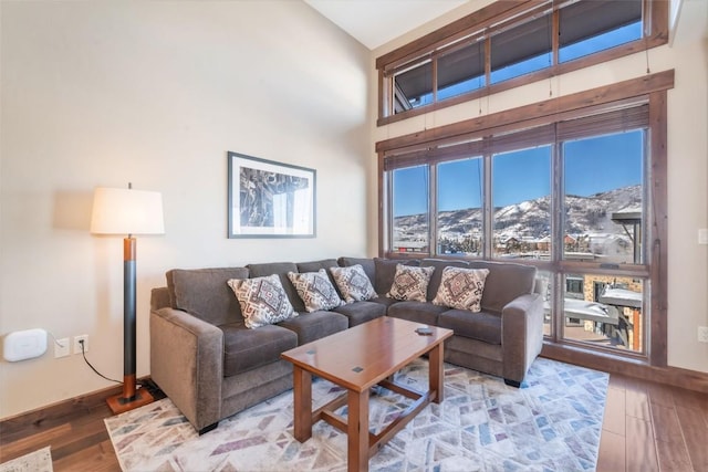 living room featuring a towering ceiling, baseboards, light wood-style floors, and a mountain view