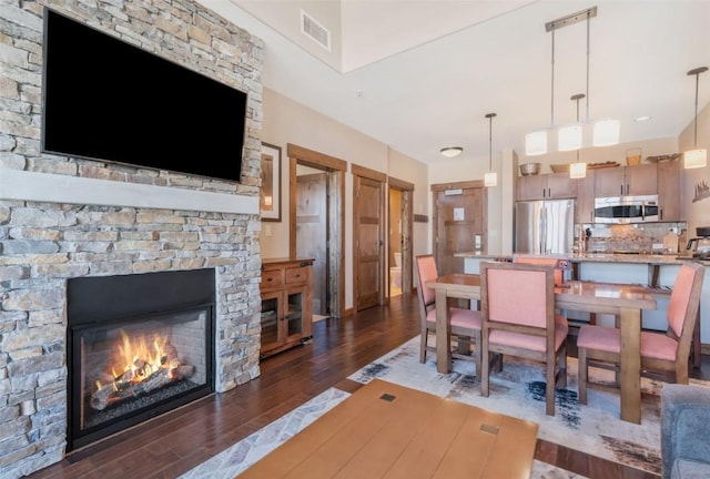 dining space with dark wood-style flooring, a stone fireplace, and visible vents