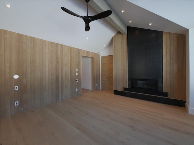 unfurnished living room with ceiling fan, a large fireplace, lofted ceiling with beams, wood walls, and light hardwood / wood-style floors