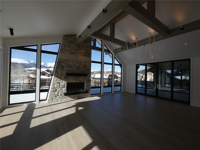 unfurnished living room with a stone fireplace, a mountain view, hardwood / wood-style floors, and lofted ceiling with beams