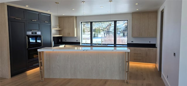 kitchen with light brown cabinets, light wood-type flooring, double oven, decorative light fixtures, and a kitchen island