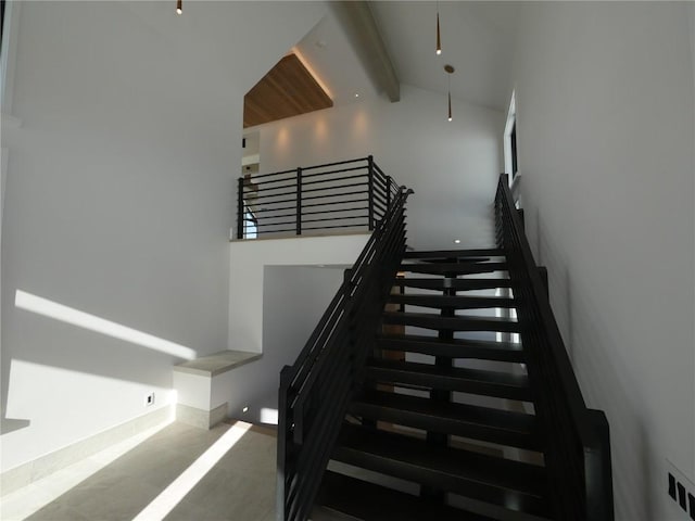 stairway featuring beamed ceiling, ceiling fan, concrete flooring, and a high ceiling