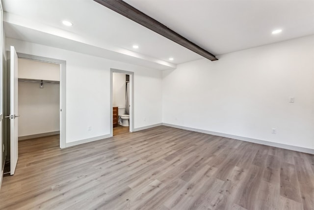 unfurnished bedroom with beamed ceiling, connected bathroom, light hardwood / wood-style floors, and a spacious closet