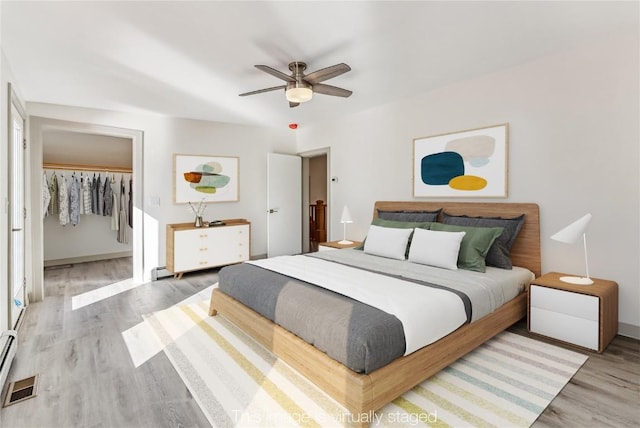 bedroom featuring hardwood / wood-style flooring, baseboard heating, a closet, and ceiling fan