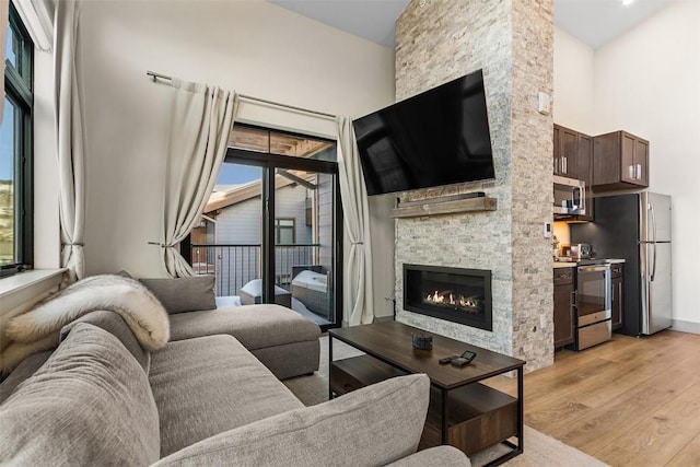 living room featuring a towering ceiling, light wood-style floors, and a fireplace