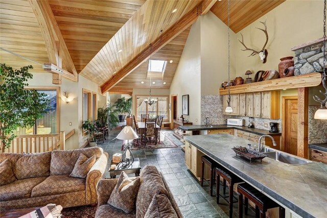 348 Jade Rd, Silverthorne, CO 80498 - living room featuring high vaulted ceiling, wooden ceiling with exposed beams, a chandelier, stone tile flooring, and a skylight
