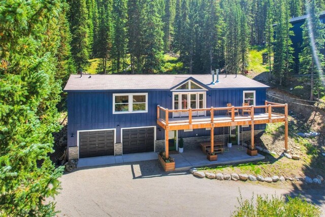 476 County Road 674, Breckenridge, CO 80424 - view of front of home featuring stone siding, an attached garage, a wooden deck, driveway, and a wooded view