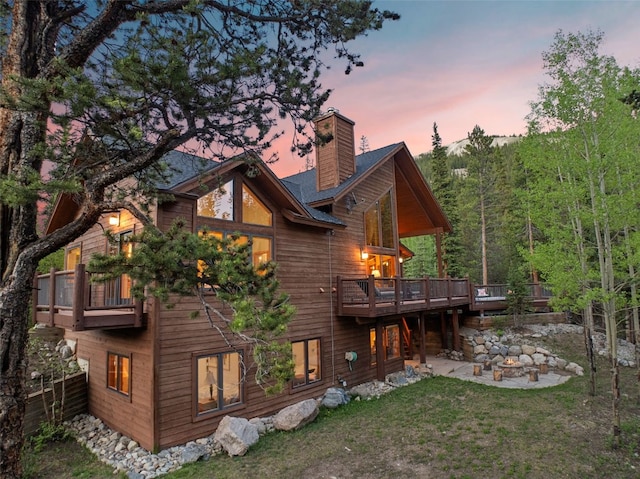 back of property featuring a wooden deck, a patio area, a lawn, and a chimney