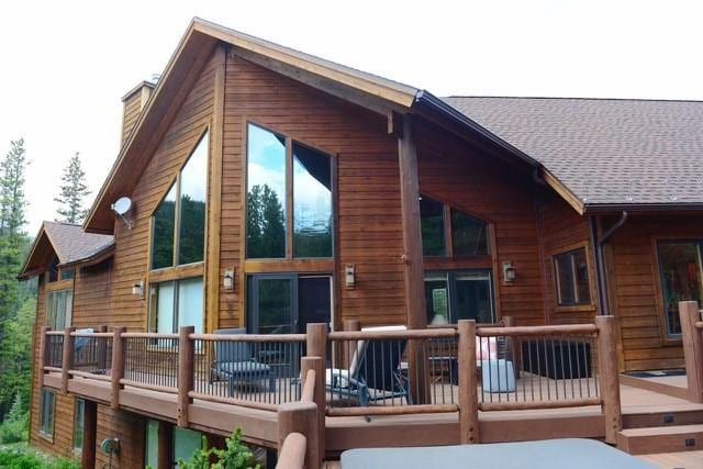 back of house with a wooden deck, a shingled roof, and a chimney