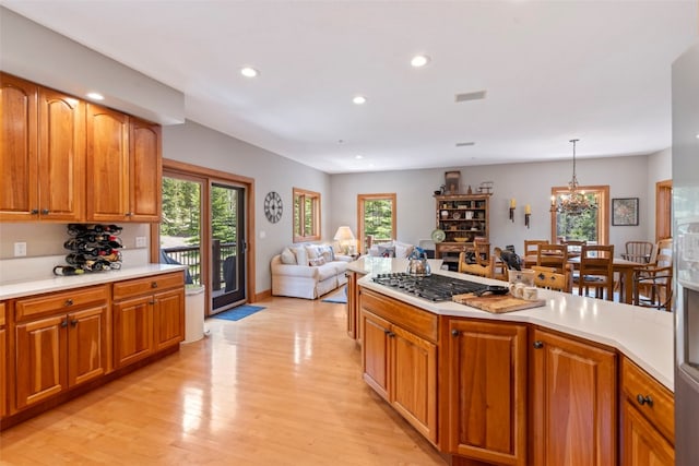 kitchen with stainless steel gas cooktop, light countertops, an inviting chandelier, and light wood-style floors