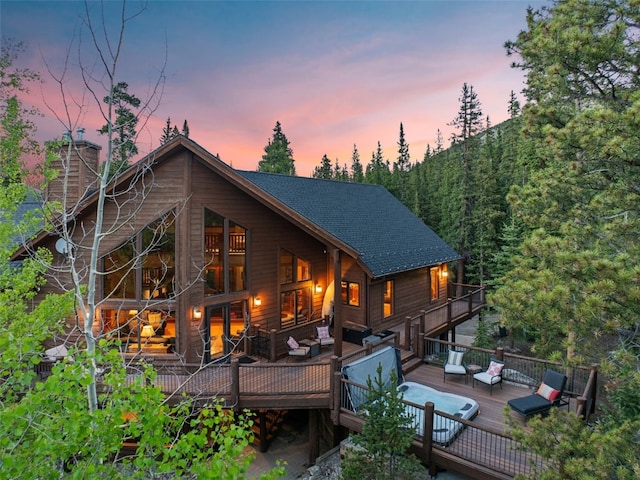 rear view of house with a deck, a shingled roof, a chimney, and an outdoor living space