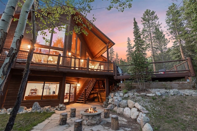 back of property at dusk with a wooden deck, an outdoor fire pit, stairs, and a patio