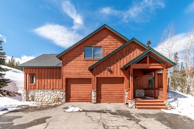 rustic home featuring driveway, stone siding, a garage, a shingled roof, and board and batten siding