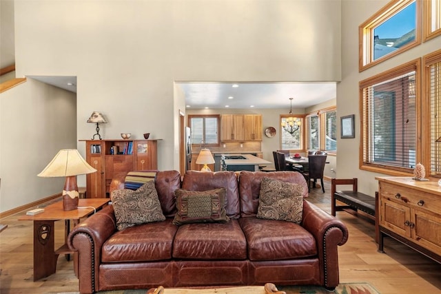 living area featuring baseboards, light wood-style flooring, a towering ceiling, and recessed lighting