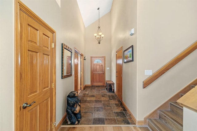 interior space featuring baseboards, a chandelier, stone finish floor, stairway, and high vaulted ceiling