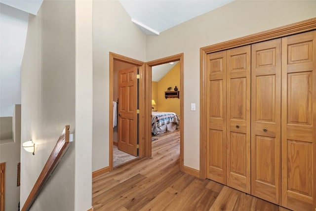 hallway with baseboards, lofted ceiling, an upstairs landing, and light wood-type flooring