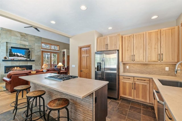 kitchen with stainless steel appliances, light brown cabinets, a sink, a fireplace, and open floor plan