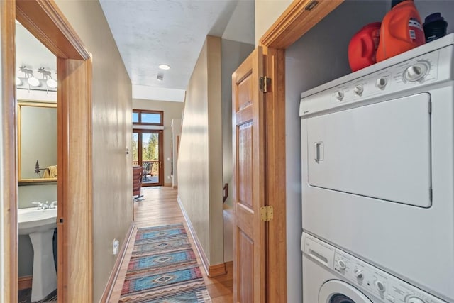 clothes washing area with a sink, light wood-type flooring, baseboards, stacked washer and clothes dryer, and laundry area