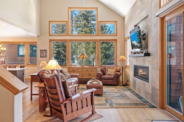 interior space featuring light wood-style floors, plenty of natural light, a tile fireplace, and high vaulted ceiling