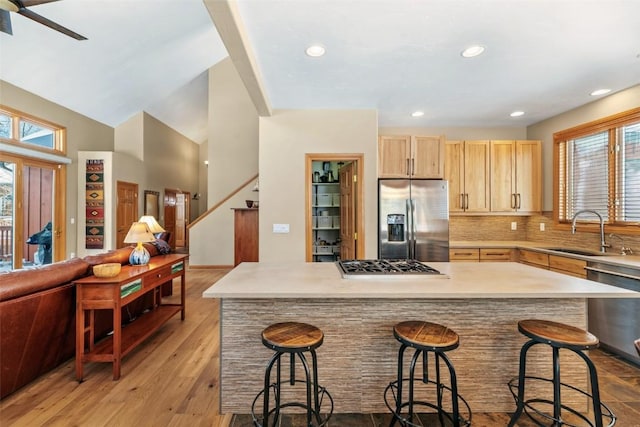 kitchen featuring stainless steel appliances, backsplash, light brown cabinets, a sink, and open floor plan