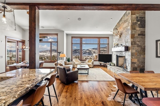 living area featuring vaulted ceiling with beams, wood finished floors, and a stone fireplace